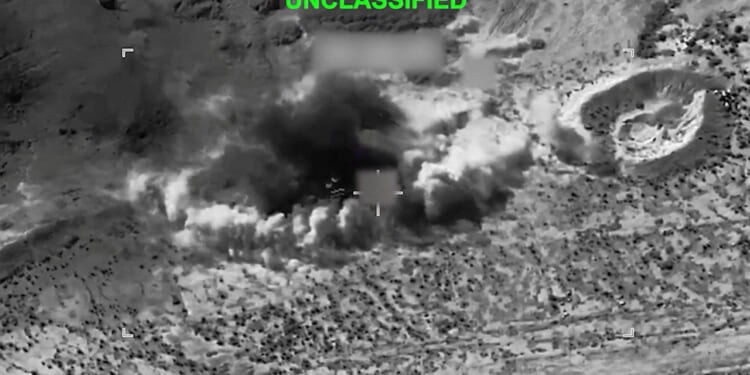 Black-and-white aerial view shows a large explosion with smoke billowing from the ground in a rugged, desert-like landscape. The word UNCLASSIFIED is displayed at the top in green text.