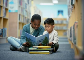 Children sit on the floor of a library as they read fairy tale books together.