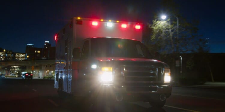An ambulance driving through a downtown district at night.