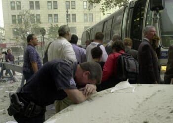 An exhausted police officer rests on a car covered in dust near the World Trade Center on Sept. 11, 2001, in New York as people board a bus to be evacuated after two hijacked planes crashed into the landmark towers.