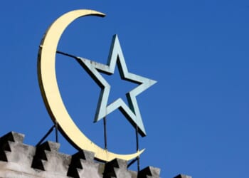 A crescent moon and star symbol is pictured on top of a building in the daylight.