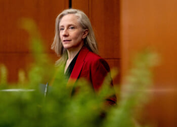 Virginia Gov. Abigail Spanberger, wearing a red blazer, stands indoors near a wall with green plants in the foreground.