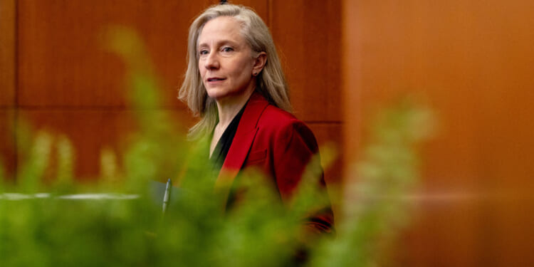 Virginia Gov. Abigail Spanberger, wearing a red blazer, stands indoors near a wall with green plants in the foreground.