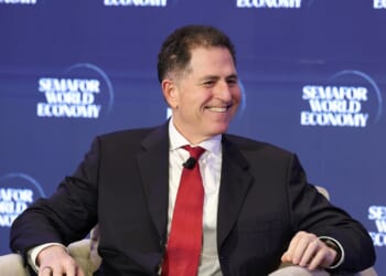 A man in a suit and red tie smiles while seated on stage at the Semafor World Economy event, with the events blue logo backdrop behind him.