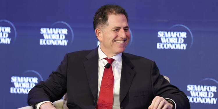 A man in a suit and red tie smiles while seated on stage at the Semafor World Economy event, with the events blue logo backdrop behind him.