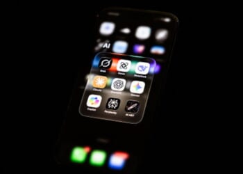 A phone screens displays AI apps on their user interface in a dark space.