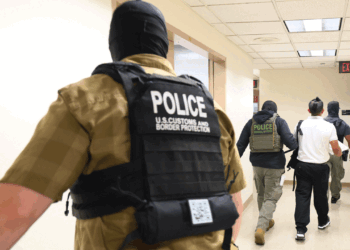 Several officers, including U.S. Customs and Border Protection, escort two individuals down a hallway in a government building.