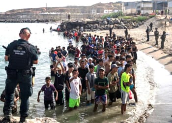 Members of the Guardia Civil USECIC guard migrants on Tarajal beach after they crossed the border between Spain and Morocco on July 31 in Ceuta, Spain.