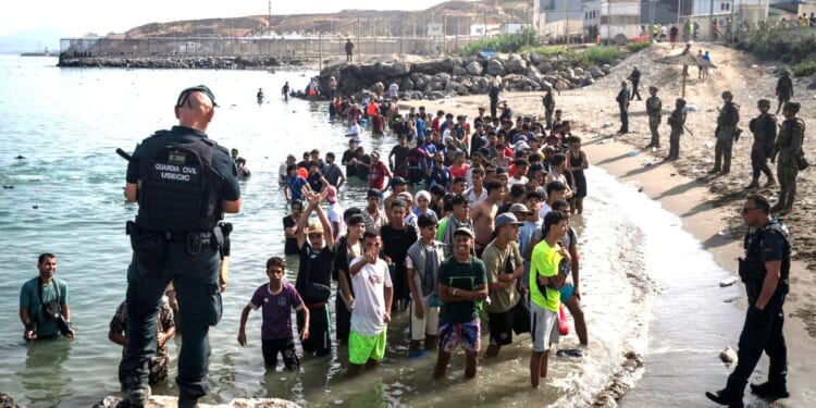 Members of the Guardia Civil USECIC guard migrants on Tarajal beach after they crossed the border between Spain and Morocco on July 31 in Ceuta, Spain.