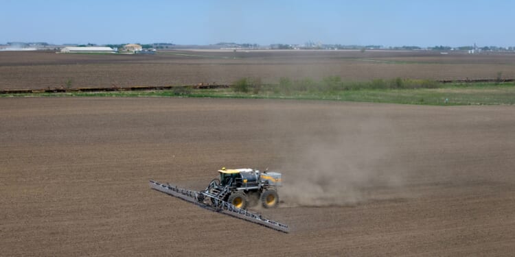 In an aerial view, a farmer applies a pre-emergent herbicide to a recently-planted corn field on May 7, 2026, near Mason City, Iowa.