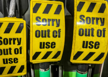 Three yellow signs with black stripes read Sorry out of use, covering the handles of fuel pumps at a gas station, indicating they are not available for service.