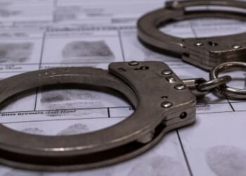 A pair of handcuffs sit on top of a fingerprinting chart in a dimly lit room.