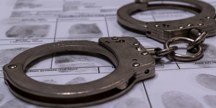 A pair of handcuffs sit on top of a fingerprinting chart in a dimly lit room.