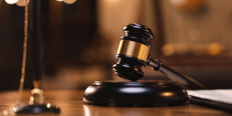 A gavel lays on a wooden block on a wooden table in a dimly lit room.