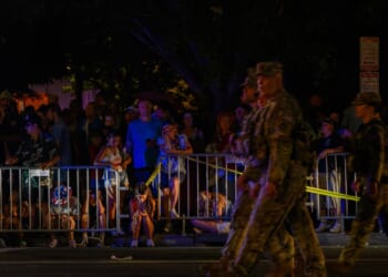 National Guard walk past people sitting on the road after being evacuated from The Great American State Fair along the National Mall due to severe weather storms forecasted to arrive in the area on July 4, 2026, in Washington, D.C.