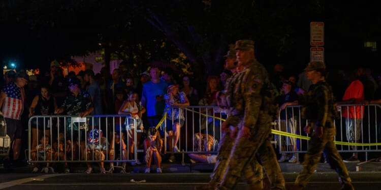 National Guard walk past people sitting on the road after being evacuated from The Great American State Fair along the National Mall due to severe weather storms forecasted to arrive in the area on July 4, 2026, in Washington, D.C.