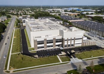 Aerial view of a large, modern data center building with the Cologix logo, surrounded by parking lots, roads, trees, and nearby industrial and residential areas.