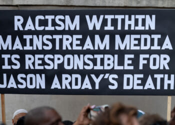 A black sign with white lettering holds "Racism within mainstream media is responsible for Jason Arday's death."