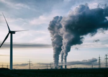 Plumes of smoke blow from a factory near a wind turbine.
