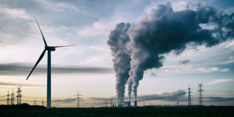 Plumes of smoke blow from a factory near a wind turbine.