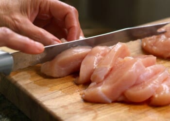 A close-up shot of a woman cutting raw chicken.