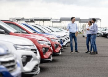 A young couple looks at cars on a car dealership lot.