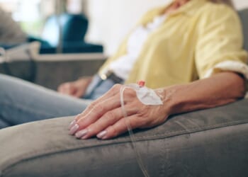 A cancer patient sits in a chair with an IV drip hooked up to her hand.