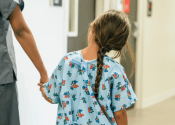 A young girl in a hospital gown with a braid walks hand-in-hand with a healthcare worker down a hallway. (Getty Images)