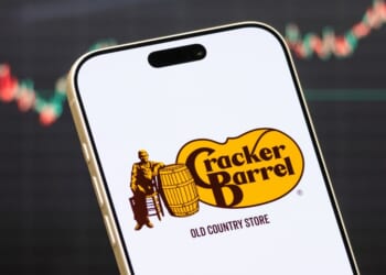 A Cracker Barrel logo displayed on a phone in front of a stock market chart.
