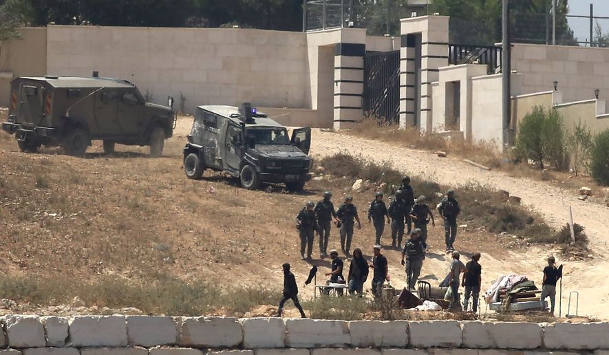 Israeli soldiers stand guard next to settlers in front of Palestinian homes that they have blockaded in the village of Qusra, south of Nablus, in the occupied West Bank, Wednesday, Aug. 12, 2026. (AP Photo/Nidal Eshtayeh)