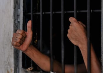 A prisoners hands are reaching from behind cell bars.