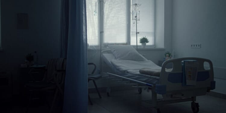 A hospital bed sits empty in a corner.