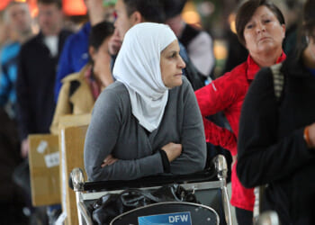 Conservatives can only effectively combat Islamism if we also defend Muslims' religious freedom. The Dallas airport foot washing controversy highlights this key distinction. Pictured: A woman in a white headscarf and gray sweater sits in a wheelchair in an airport, surrounded by people in line. The wheelchair has a DFW sign on it.