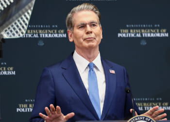 The man who tried to assassinate Treasury Secretary Scott Bessent identifies as transgender and was sentenced to a prison term. Pictured: Bessent, a man in a blue suit and glasses speaks at a podium with his hands raised, standing in front of a backdrop that reads The Resurgence of Political Terrorism.