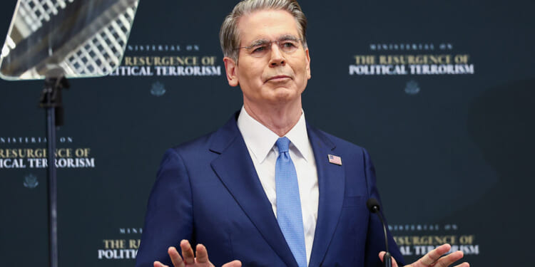 The man who tried to assassinate Treasury Secretary Scott Bessent identifies as transgender and was sentenced to a prison term. Pictured: Bessent, a man in a blue suit and glasses speaks at a podium with his hands raised, standing in front of a backdrop that reads The Resurgence of Political Terrorism.