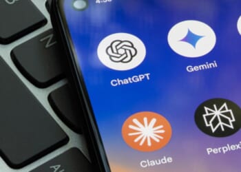 A phone screen displaying artificial intelligence apps lays on top of a laptop keyboard.