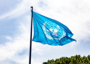 The United Nations flag waves in the sky.