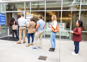 People stand in a line outside a polling center during the day.