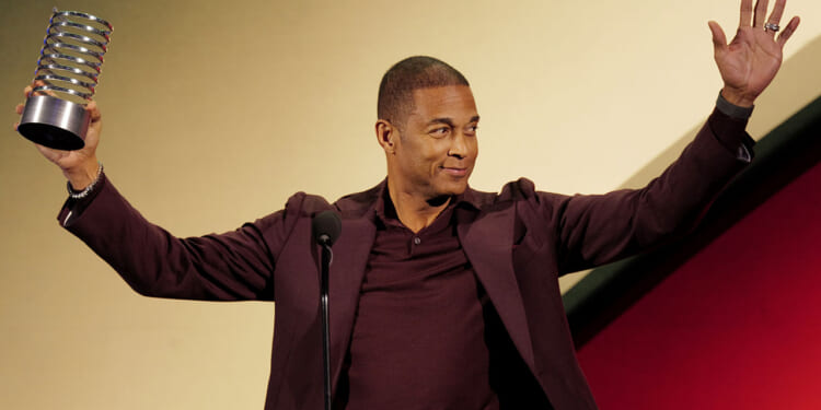 Former CNN host Don Lemon is trying to overturn part of the FACE Act. Pictured: a man in a maroon suit stands at a microphone, smiling and raising both arms. He holds a spiral-shaped award trophy in his left hand against a yellow and red background.