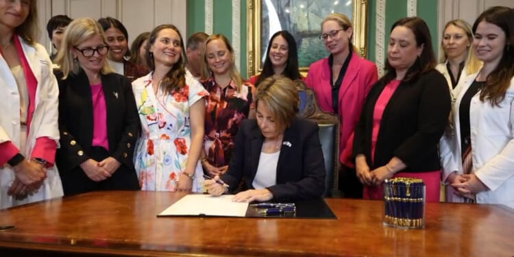 Massachusetts Governor Maura Healey signed the bill, surrounded by grinning, giggling females.