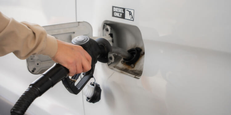 A person’s hand refueling a vehicle with a diesel pump nozzle at a gas station, highlighting the importance of diesel as both a local fuel source and in global markets through diesel exports. The fuel door has a label that reads Diesel Only.