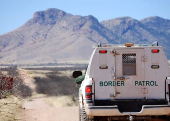 The back of a border patrol truck driving on a dirt road along the Mexican border in Arizona, with mountains in the background.