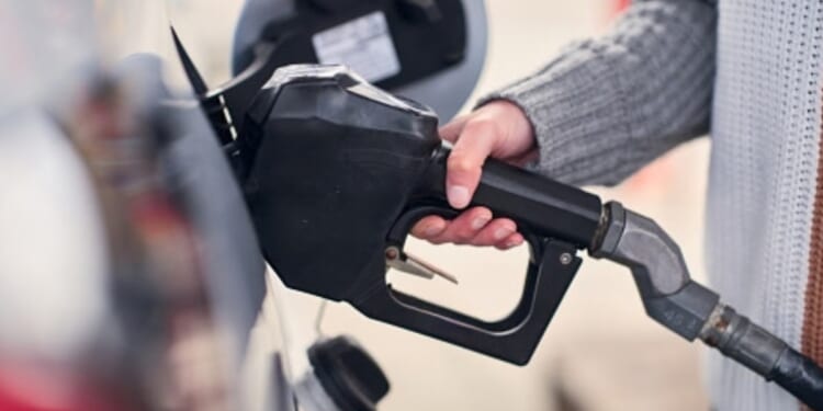 A woman grabs gas pump at a gas station.