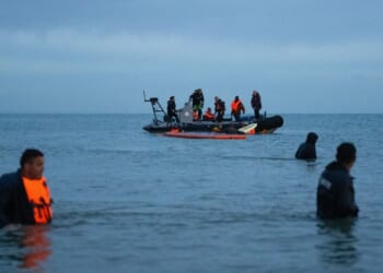 A French rescue vessel patrols next to migrants wading in the sea after failing to board a dinghy to cross into the English Channel on June 30, 2026, in Wissant, France.