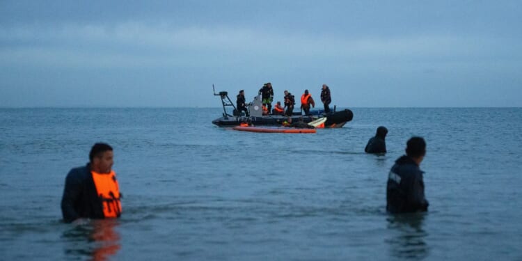 A French rescue vessel patrols next to migrants wading in the sea after failing to board a dinghy to cross into the English Channel on June 30, 2026, in Wissant, France.