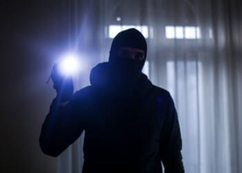 A burglar shines a bright flashlight in a dark house.