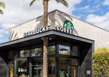 A modern Starbucks Coffee building with a palm trees and a blue sky.