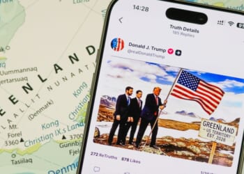 A photo illustration shows a smartphone displaying a post from the Truth Social account of President Donald Trump over a map of Greenland in the background.