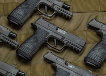 Pistols are laid out on a brown fabric in a pattern.