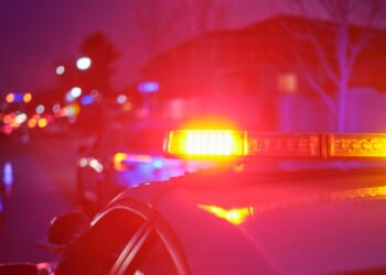 A police car at night alongside a road with emergency lights flashing.